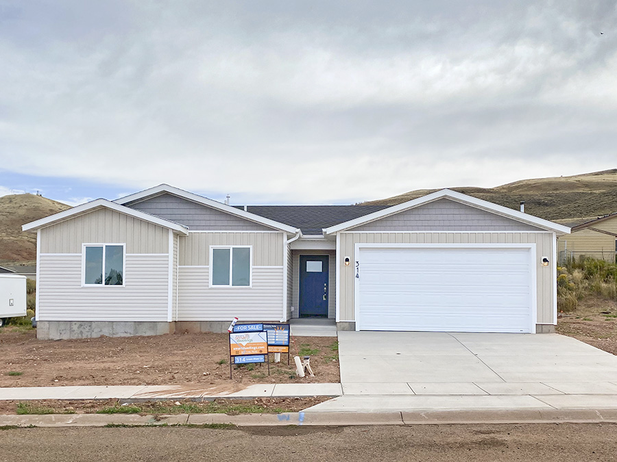 Tan and grey ranch home with blue front door and two-car garage in white. A new build of the Edison floor plan by Smart Dwellings at 314 Green River Cir in Evanston WY